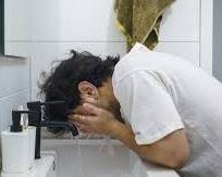 A person splashing cold water on their face in a bathroom with a fresh feeling.