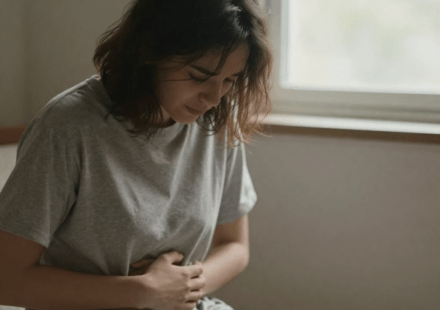 Person sitting by window looking depressed with hand on stomach showing gut health and depression connection