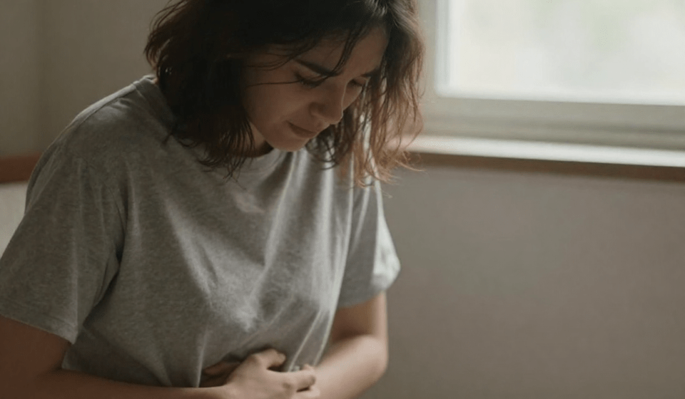 Person sitting by window looking depressed with hand on stomach showing gut health and depression connection