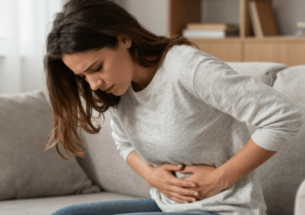 Woman sitting on couch holding stomach due to nausea from anxiety